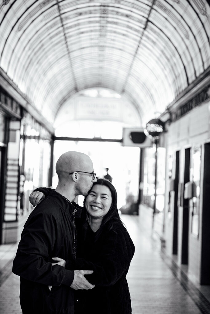 a couple hugging, partner is kissing her on the forehead as she giggles.
Engagement session in Melbourne.