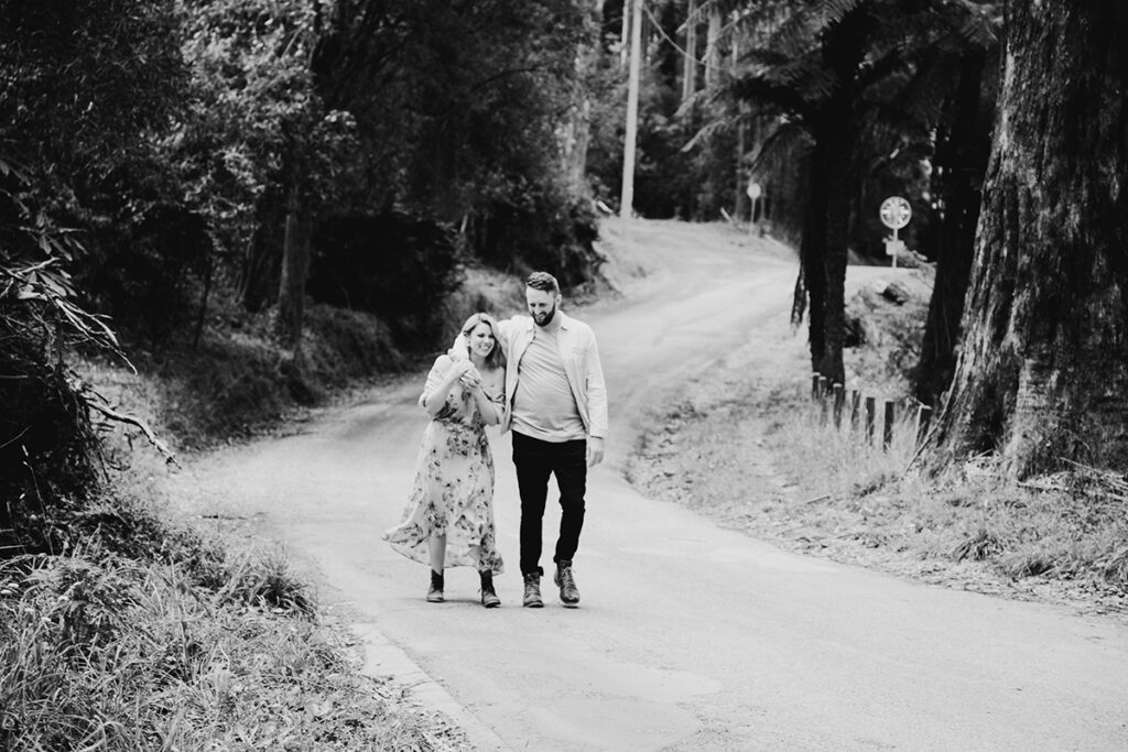 black and white photo of a couple having an engagement session. Walking up a road with an arm around each other.