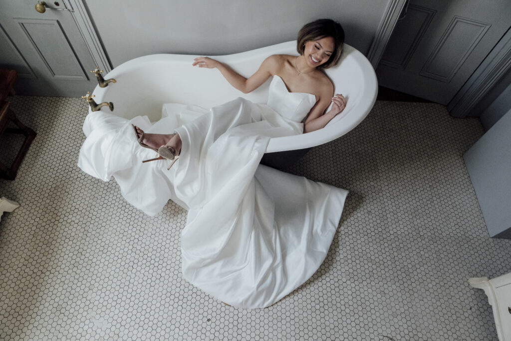 bride sitting in a bath tub in her wedding dress laughing