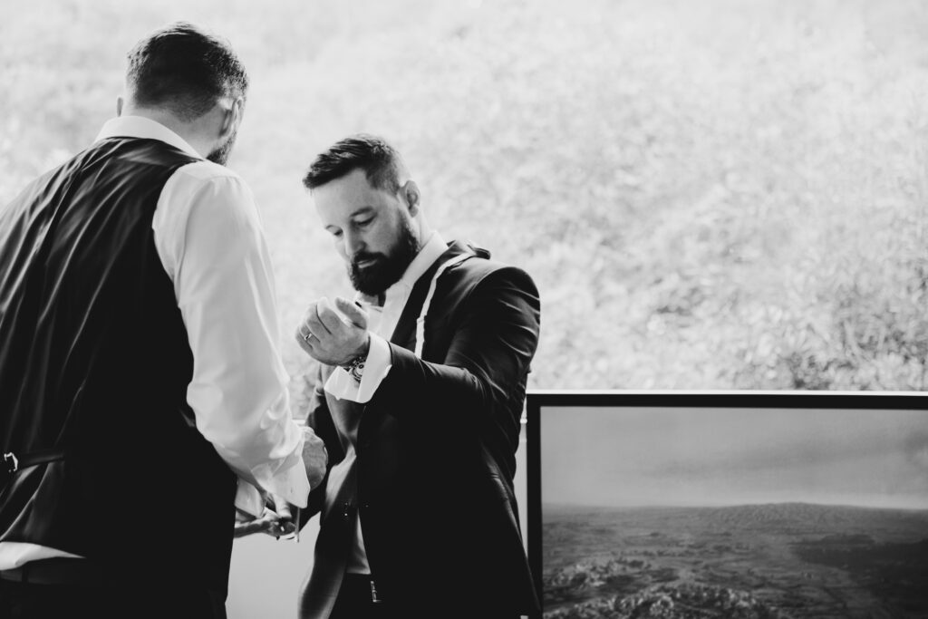 black and white image of groom and best man helping the best man do his cufflinks.
