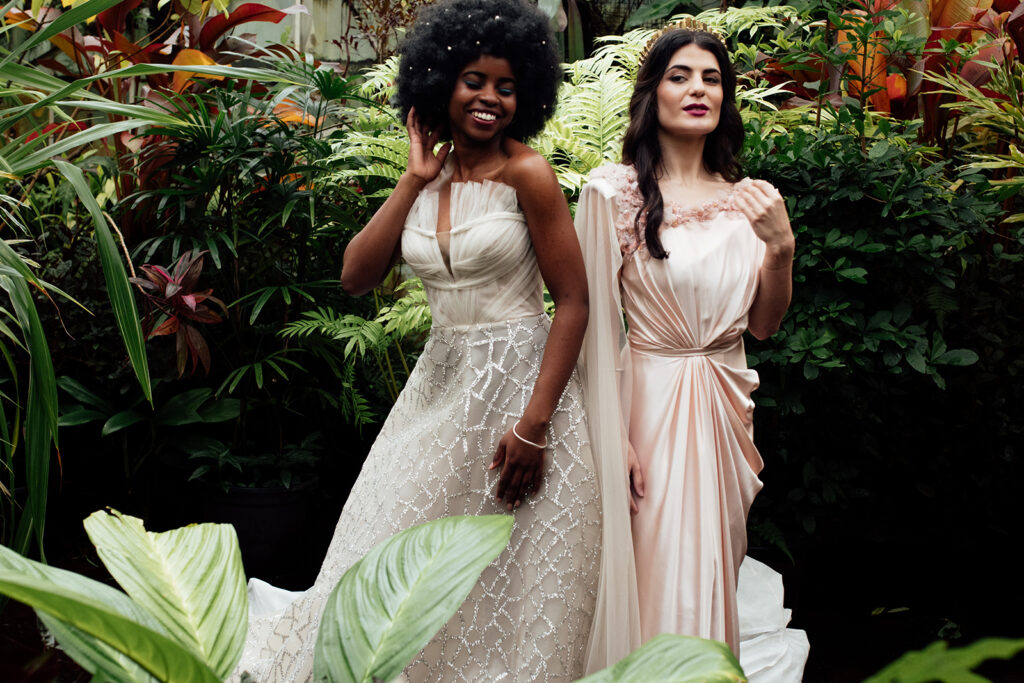 Colour image of 2 girls standing in a greenhouse wearing gorgeous gowns after having their makeup done by one of the best wedding makeup artists in Melbourne. Photograph taken by Liminal wonderland wedding Photographer