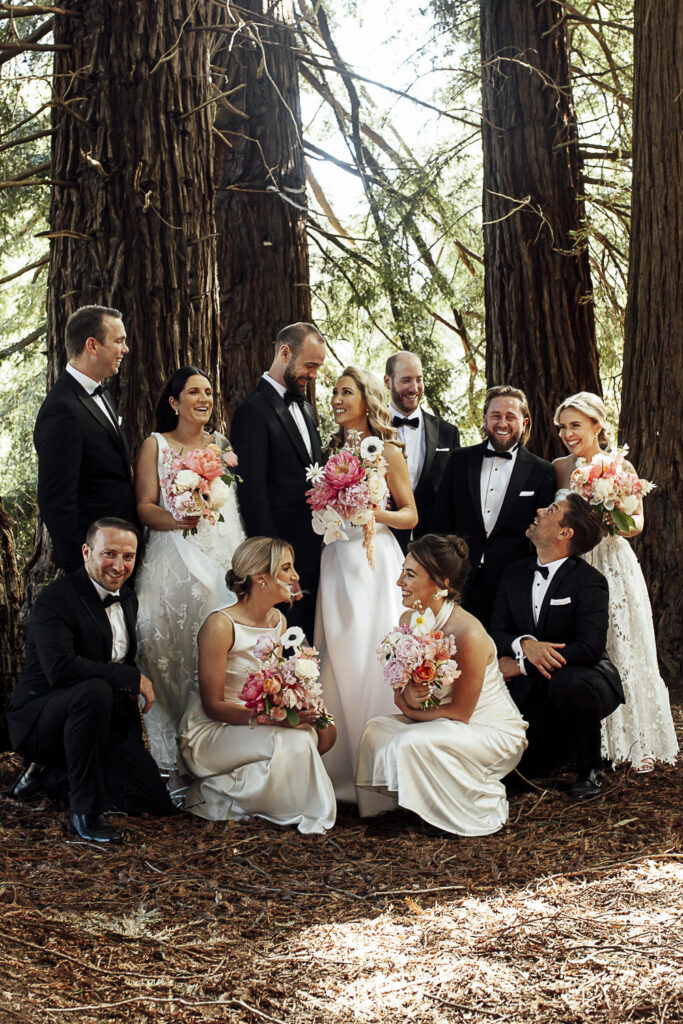 Wedding photo in the redwood forrest. a Bride and groom stand still as the bridal party are surrounding them.