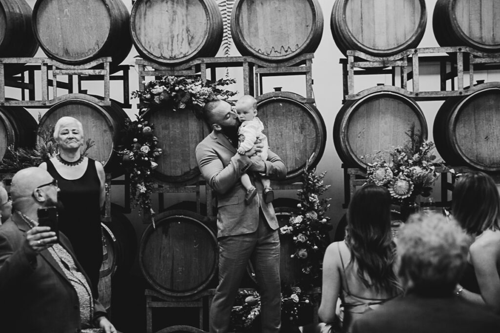 a black and white image of a groom holding a baby at the end of the aisle 