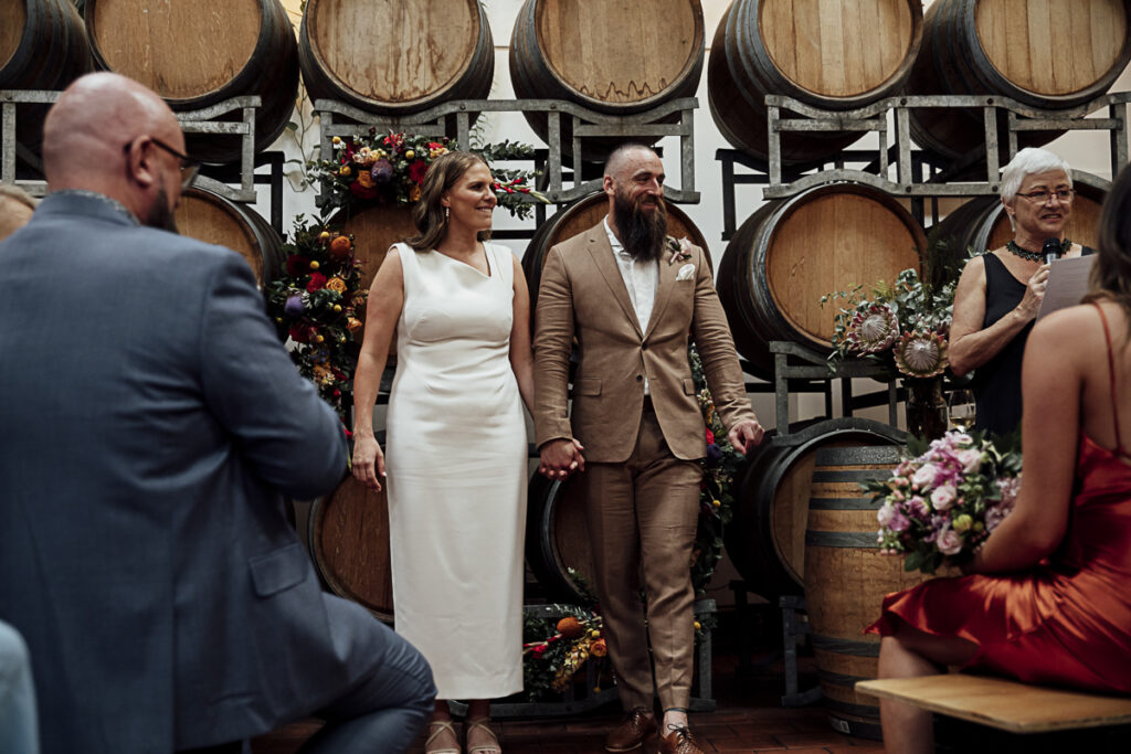 a bride and groom standing in front giant wine barrels at a wedding ceremony
