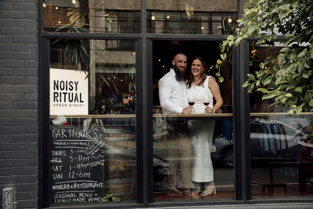 A bride and groom standing at a window sharing a glass of wine at Noise Ritual