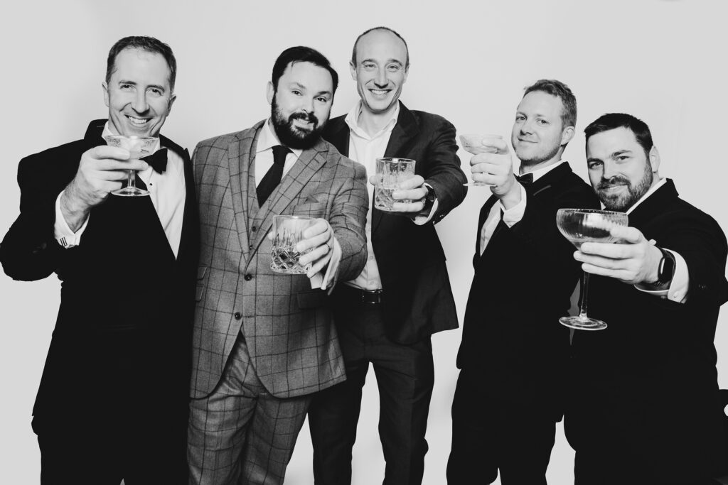 A black and white photo of a group of boys having fun clicking her glass having a photo taken