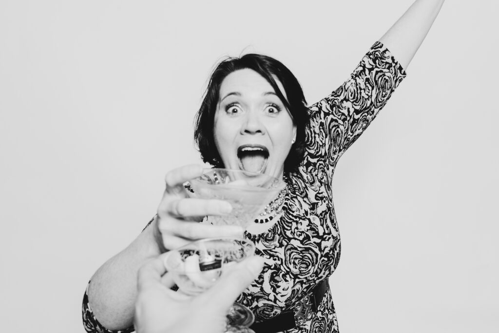 A black adn white photo of a girl having fun clicking her glass having a photo taken