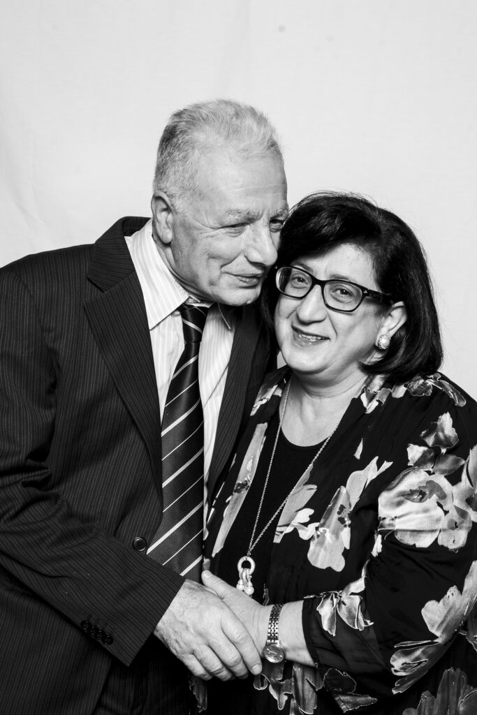 A black and white photo of an older couple standing in a portrait studio haveing a picture taken