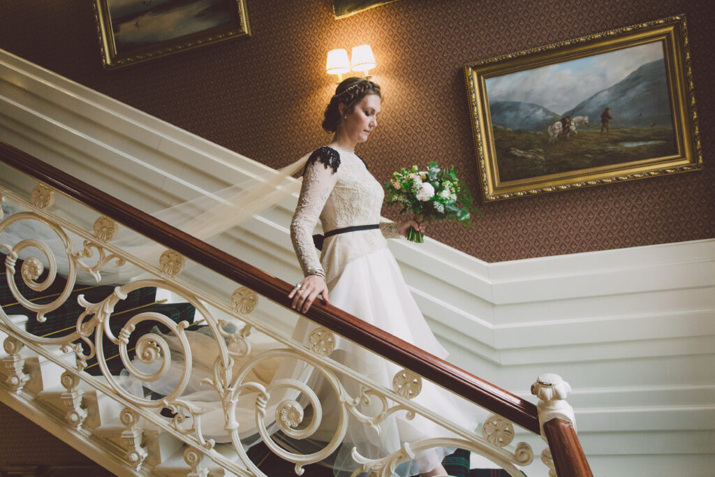 An image of a bride walking down the stairs to Drumtochy castle in a custom one of a kind wedding dress.