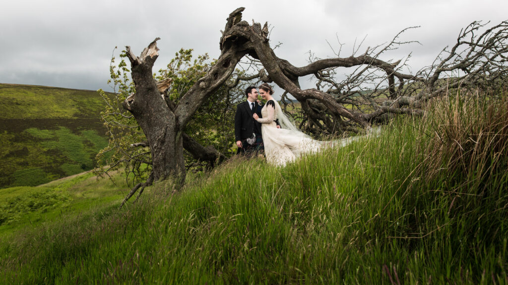 a couple on their wedding day having photos taken in Scotland. She's wearing a custom wedding dress with tulle and a cape veil very flowy