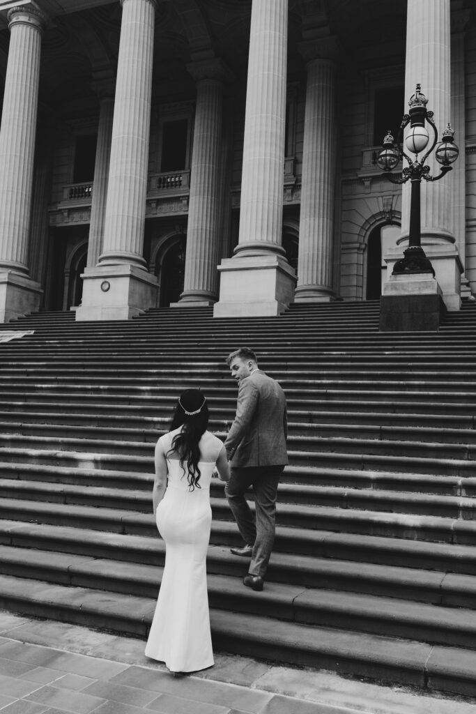 Black and White image of A couple having a Melbourne Elopement, walking up the steps of Parliament 