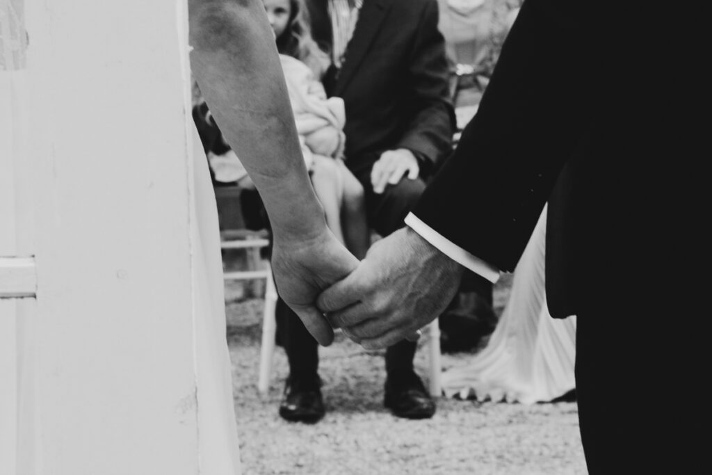 A black and white image of a bride and groom holding halds.