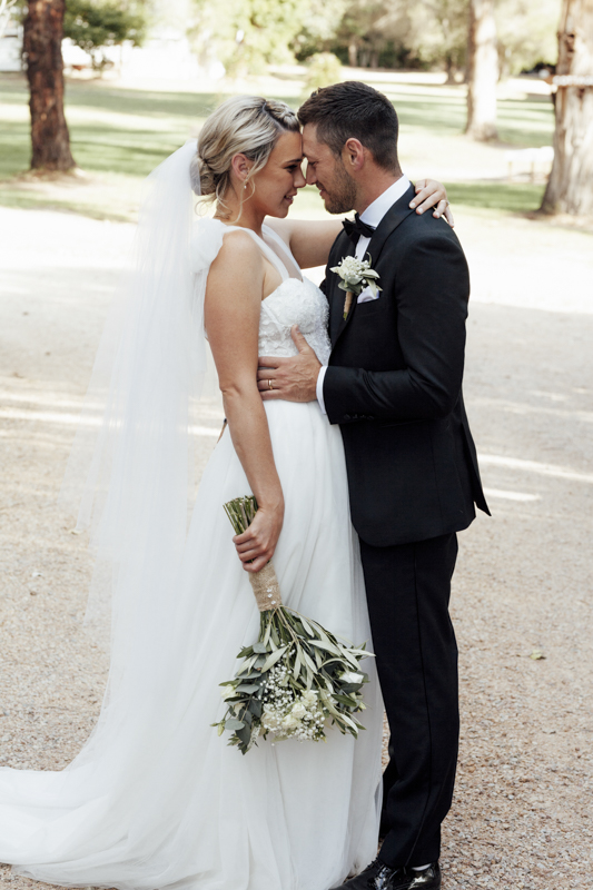 A colour image of a bride and groom having professional wedding photos taken at eight acres lakes entrance on their wedding day.