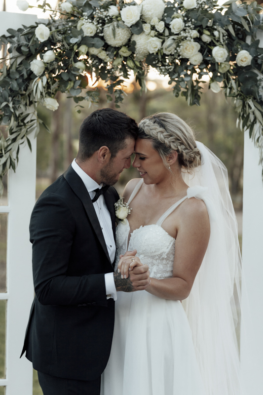 A colour image of a bride and groom having professional wedding photos taken at eight acres lakes entrance on their wedding day at sunset.