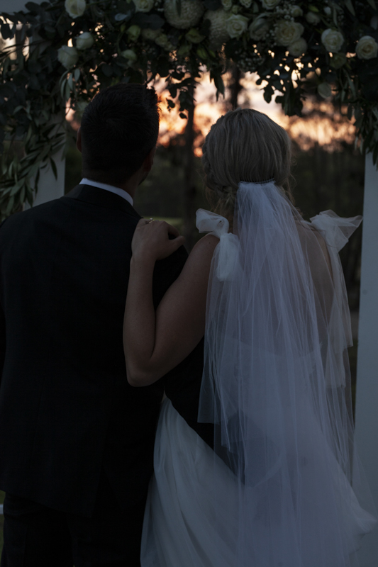 A colour image of a bride and groom having professional wedding photos taken at eight acres lakes entrance on their wedding day at sunset.