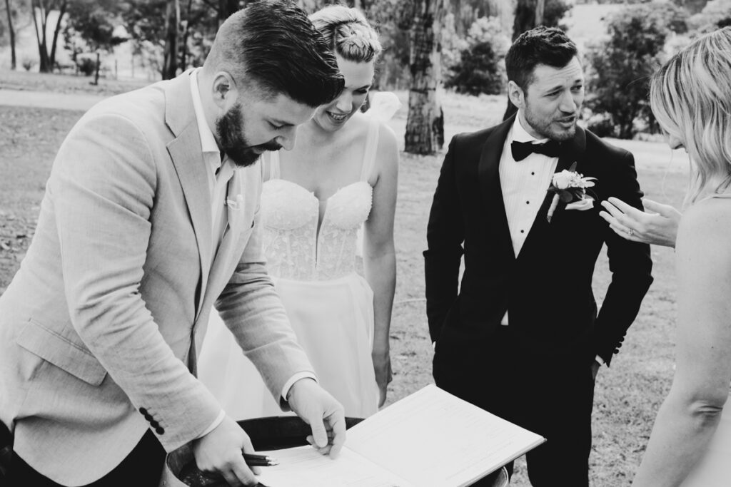 A black and white image of a bride and groom signing the registry