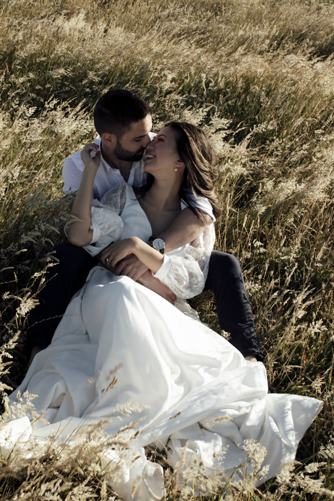 Pre-wedding photoshoot Melbourne in Flinders a couple laughing and hugging sitting in the long grass and wind swooshing