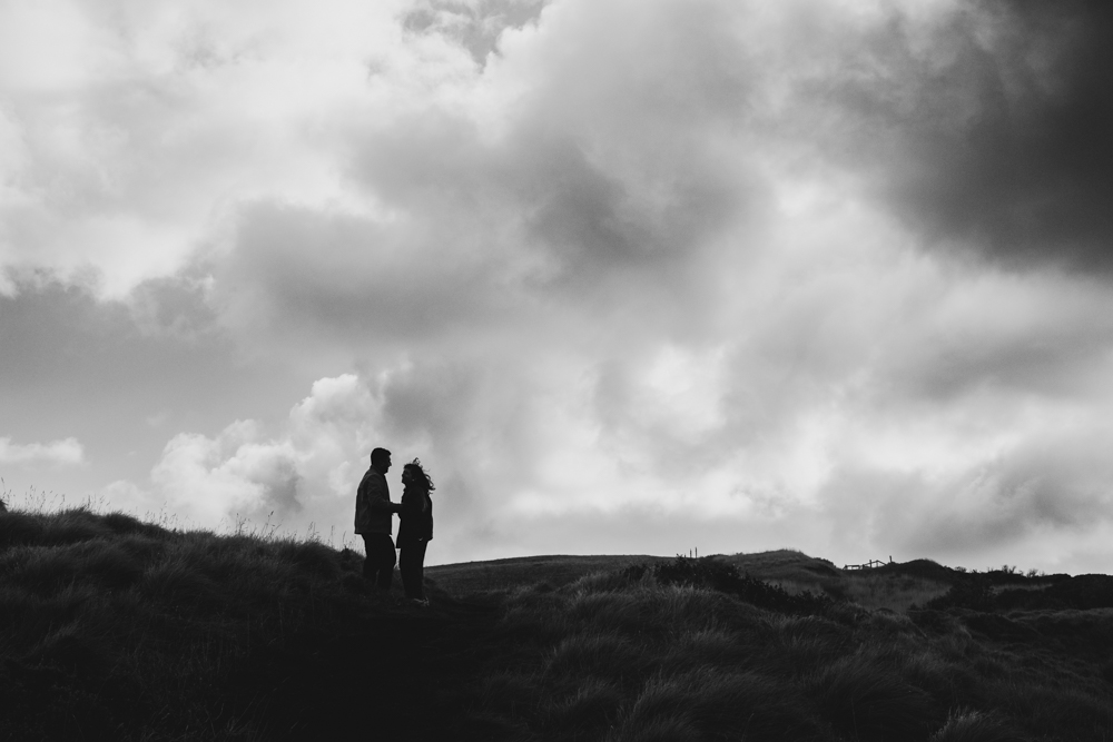 Pre-wedding photoshoot Melbourne in Flinders a couple laughing and hugging a moody black and white with clouds
