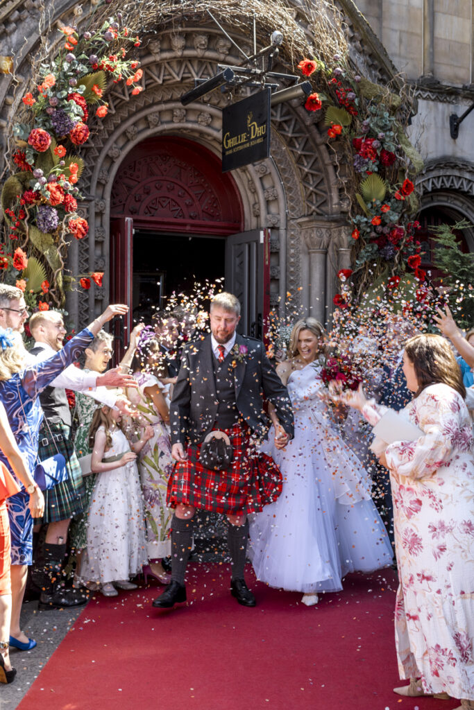 Edinburgh wedding photographer candid, a bride and groomcoming out to a wall of confetti at the Ghillie Dhu