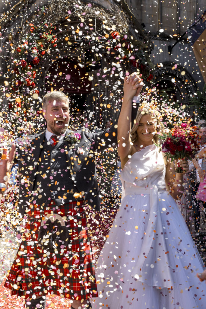 Edinburgh wedding photographer candid, a bride and groomcoming out to a wall of confetti at the Ghillie Dhu