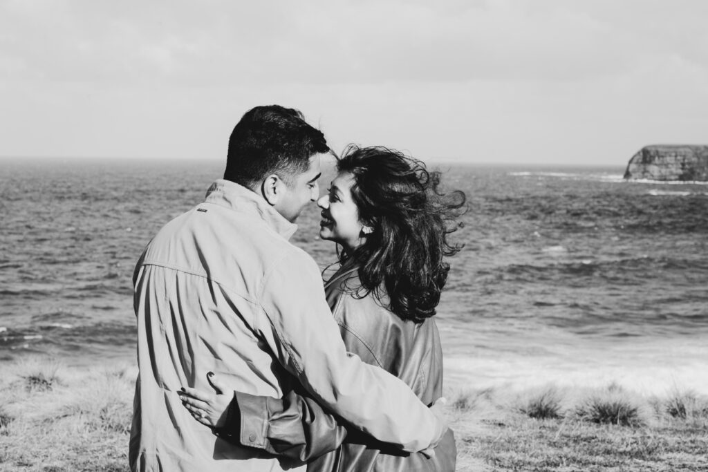 Melbourne Proposal Photography a couple getting engaged in Flinders. Young couple standing on cliff top laughing and looking at each other. The image is black and white