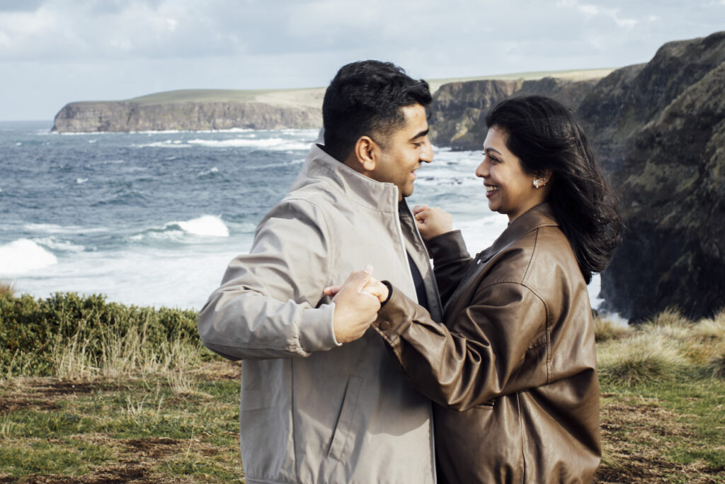 Melbourne Proposal Photography a couple getting engaged in Flinders. Young couple standing on cliff top laughing and looking at each other.