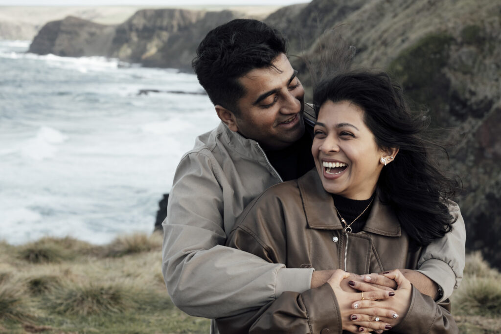 Melbourne Proposal Photography a couple getting engaged in Flinders. Young couple standing on cliff top laughing and looking at each other.