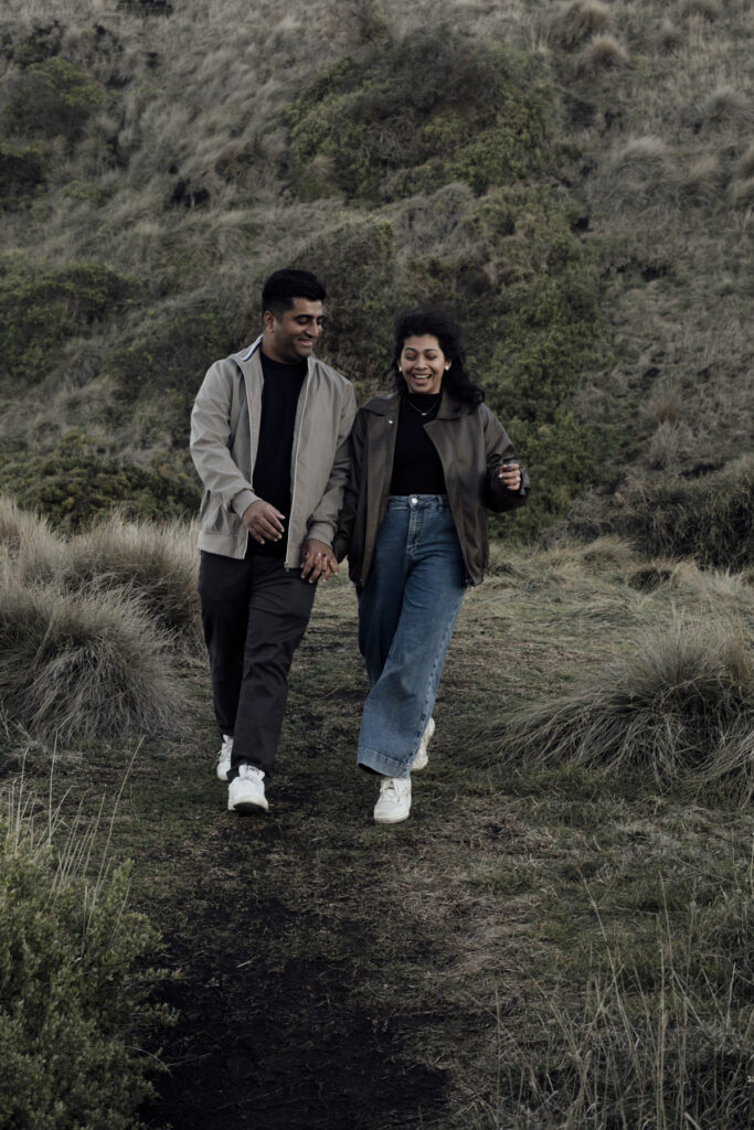 Melbourne Proposal Photography a couple getting engaged in Flinders. Young couple standing on cliff top laughing, holding hands and walking