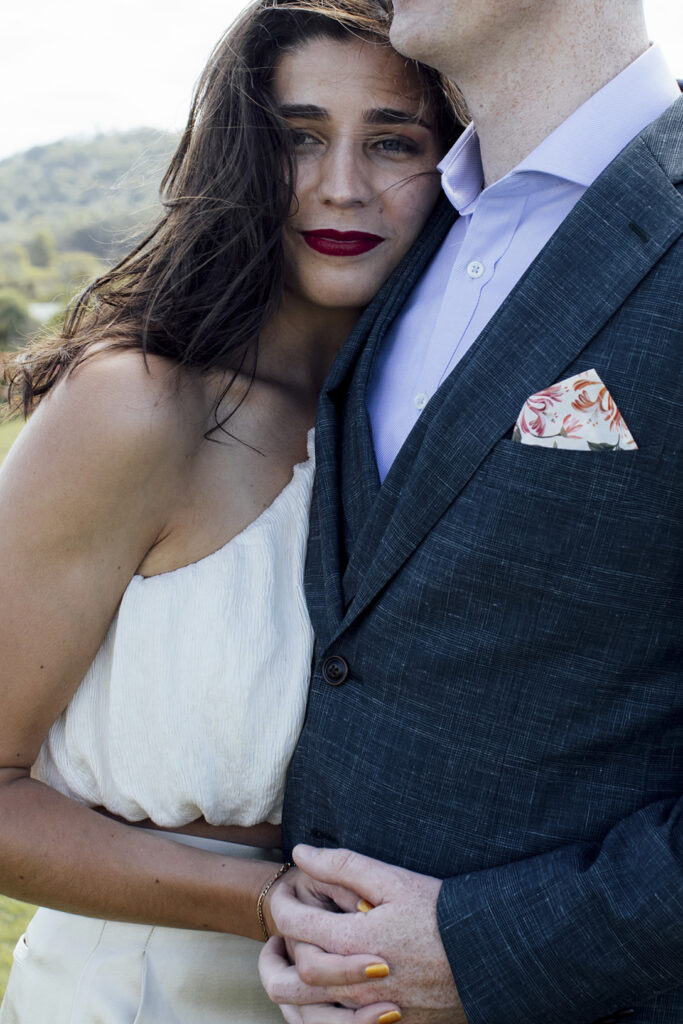 A beautiful, natural, candid image of a couple having wedding photos at Gurneys' Cider, they are close and holding hands she is looking direct at the camera. Beautiful red lip!