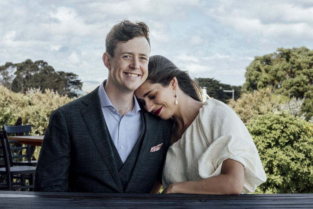 A couple having portraits at Gurney's cidery. The girl wears a beautiful gold jumpsuit, windswept hair. They are snuggly and close sitting down. Candid and beautiful wedding photos.