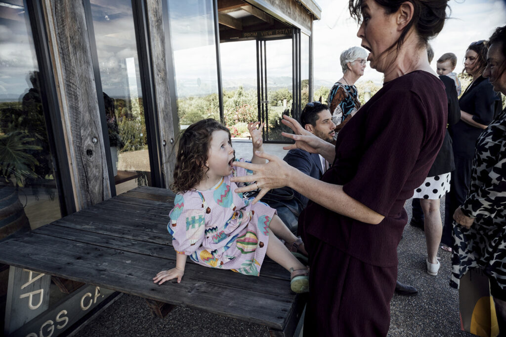 A couple having portraits at Gurney's cider. The girl wears a beautiful gold jumpsuit, windswept hair. They are snuggly and close standing the sky is dark and moody and stormy. Standing with Wilsons prom in the background.
