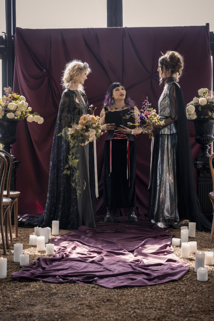 A wedding photo of two brides at Scrub Hill, they are having a spiritual led ceremony with Celebrant Jam. There is smoke and candles in the background making the image more etherial. They brides are wearing long gold silk gowns by Gwendolyn.