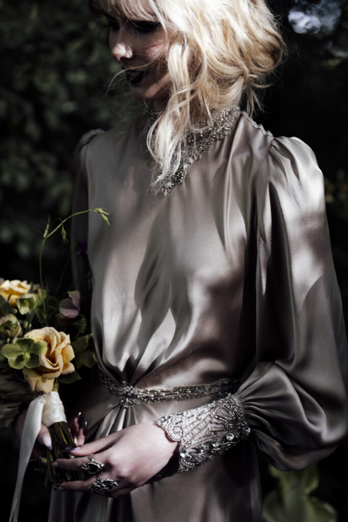 a bride walking through the forest at Scrub Hill on her wedding day, it is softly lit, alternative and etherial looking with a green hue. She is wearing a long golden silk gown with a Gatsby vibe from Gwendolyn Couture