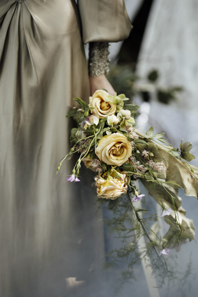 a bride walking through the forest at Scrub Hill on her wedding day, it is softly lit, alternative and etherial looking with a green hue. She is wearing a long golden silk gown with a Gatsby vibe from Gwendolyn Couture