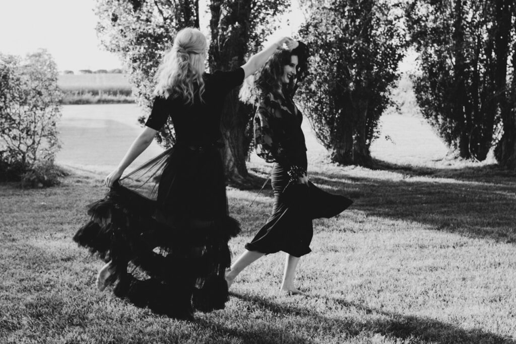a black and white photo of two brides dancing barefoot and having fun in the field at Scrub Hill on their wedding day in dayelsford.