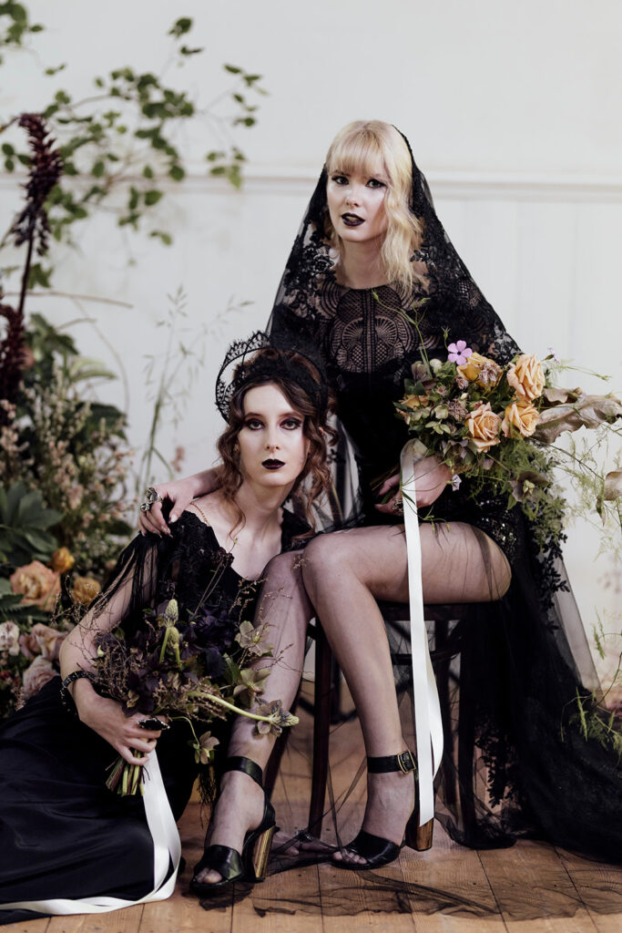 Two brides in the bluestone chapel at Scrub Hill in Dayelsford. They are alternative stunning brides. They girls are wearing black dresses and wearing a black veil and black crown.