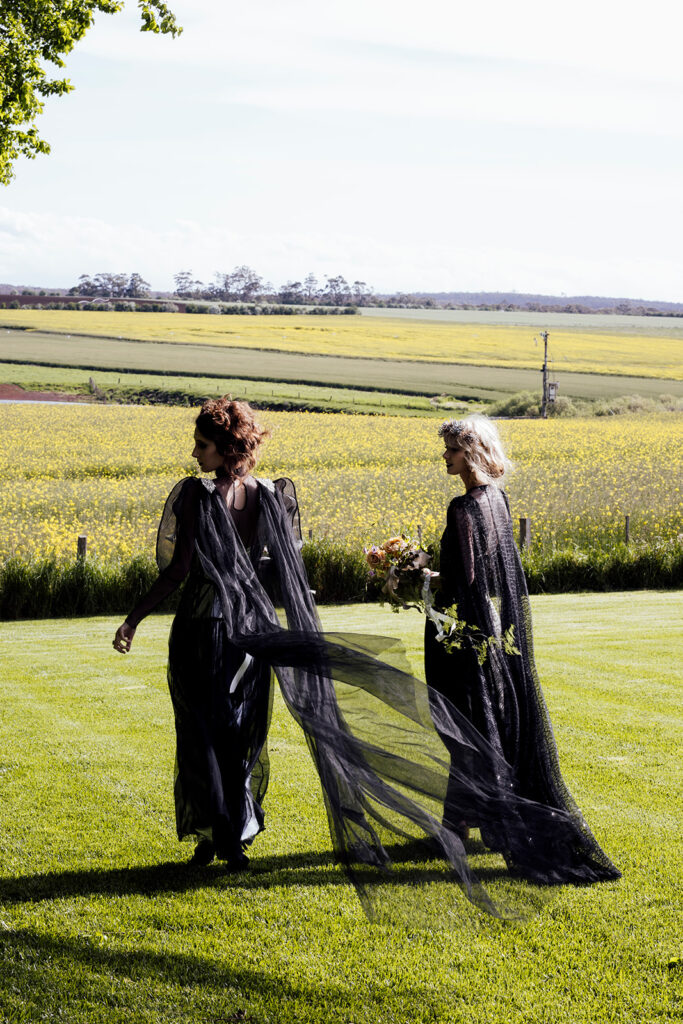 two women at a wedding in Scrub Hill, they are wearing black gowns by Gwendolyn Couture. They alos have incredible crowns by Stephanie Browne, the flowers are wild by Larkspur flowers. The setting is beautiful and summery.