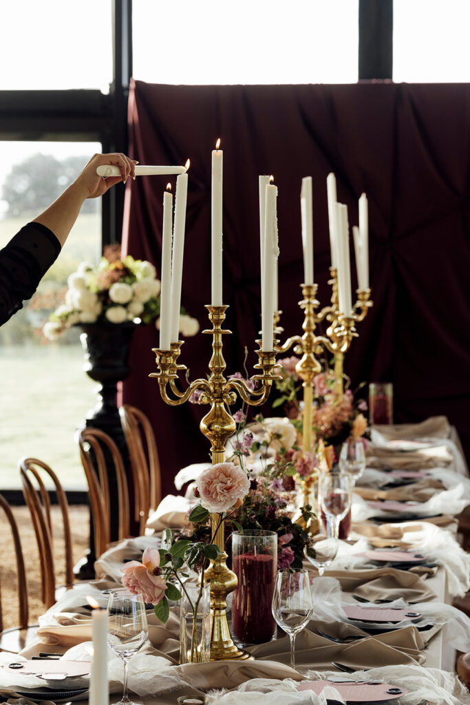 Wedding reception table setting at Scrub Hill, The table linen is silk and glowy golden, the flowers are soft and warm, candelabras line the table to give a moody vibe. The overall image is warm and lucious