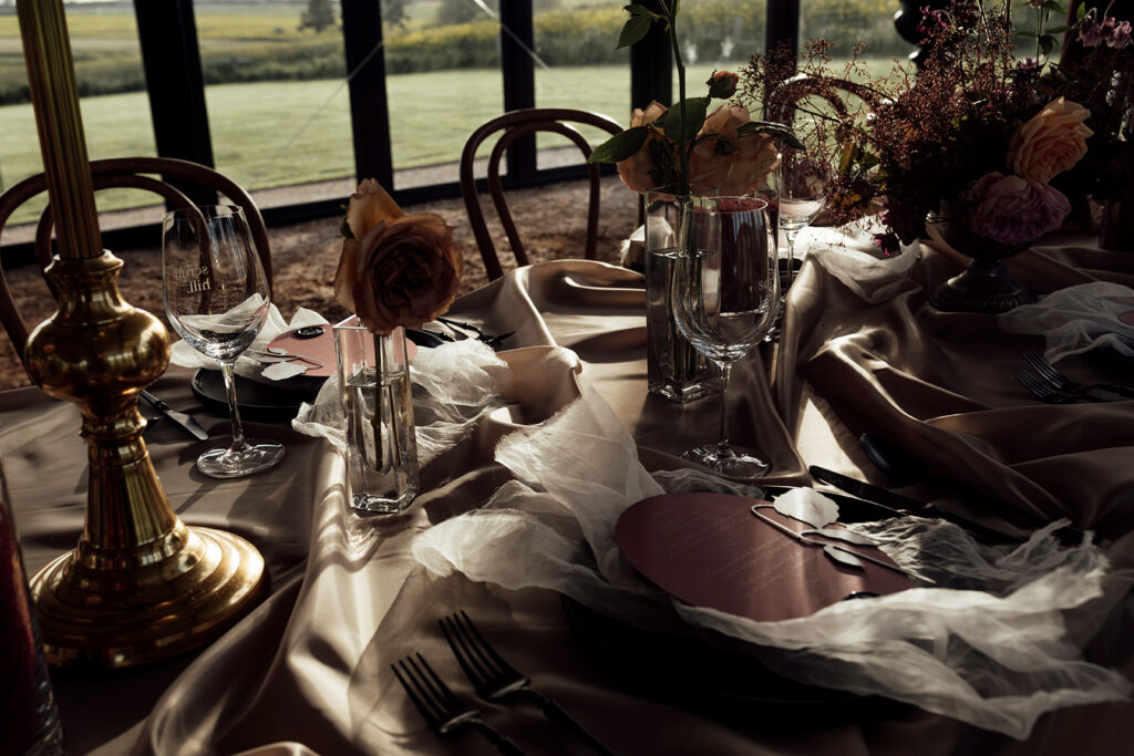 Wedding reception table setting at Scrub Hill, The table linen is silk and glowy golden, the flowers are soft and warm, candelabras line the table to give a moody vibe. The overall image is warm and lucious