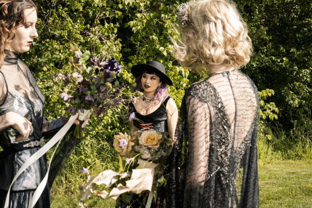 A wedding photo of two brides at Scrub Hill, they are having a spiritual led ceremony with Celebrant Jam. There is smoke and candles in the background making the image more etherial. They brides are wearing long gold silk gowns by Gwendolyn.