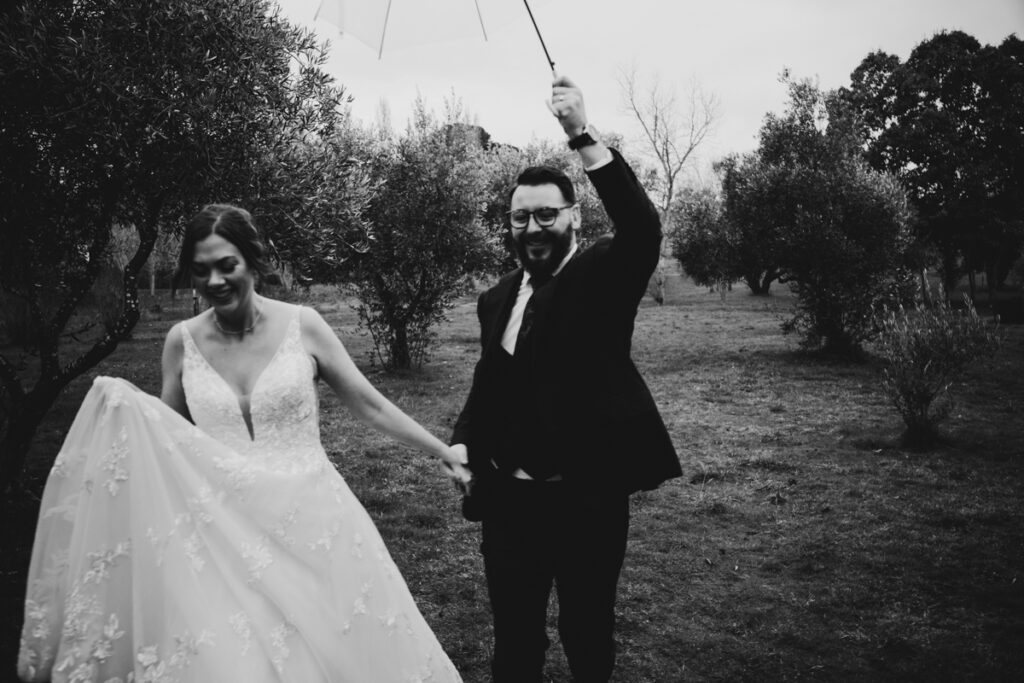 A black and white photo of a bride and groom running a dodging rain clouds on their wedding day